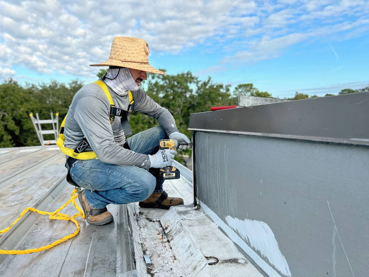 Certified Best Roofing technician in safety harness fastening flashing during a preventative maintenance visit on a commercial metal roof