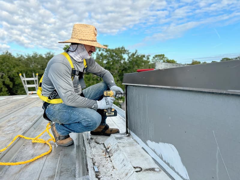 Certified Best Roofing technician in safety harness fastening flashing during a preventative maintenance visit on a commercial metal roof