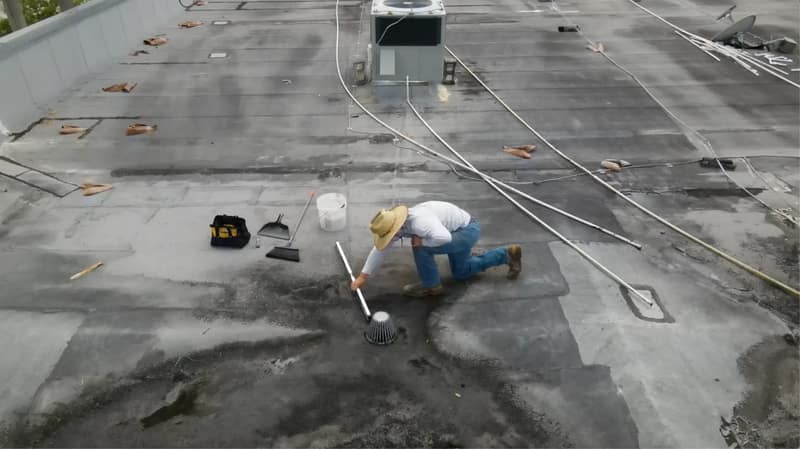 Certified Best Roofing technician clearing a roof drain on a commercial flat roof in Central Florida