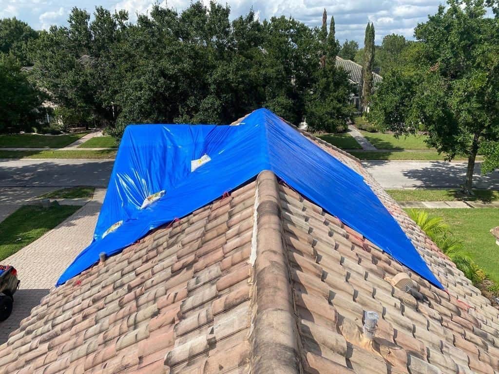 Blue emergency tarp secured over a storm-damaged tile roof in a Central Florida neighborhood