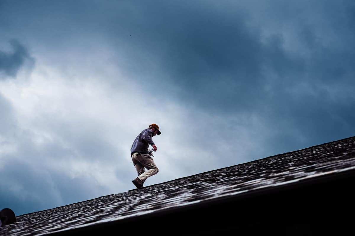 Certified Best Roofing technician inspecting a shingle roof under a dark, stormy Central Florida sky